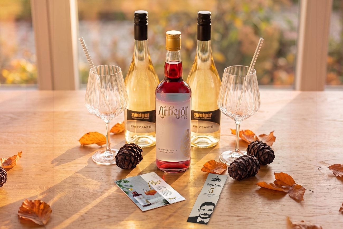 Herbst-Sprizz-Set mit Zirberol Sprizz, zwei Flaschen Frizzante, zwei Aperitifgläsern, Cocktailkarte und Gutschein auf einem Holztisch
